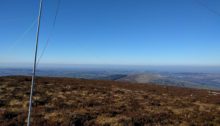 Antenna pole in forground, looking to countryside on the horizon with a blue sky