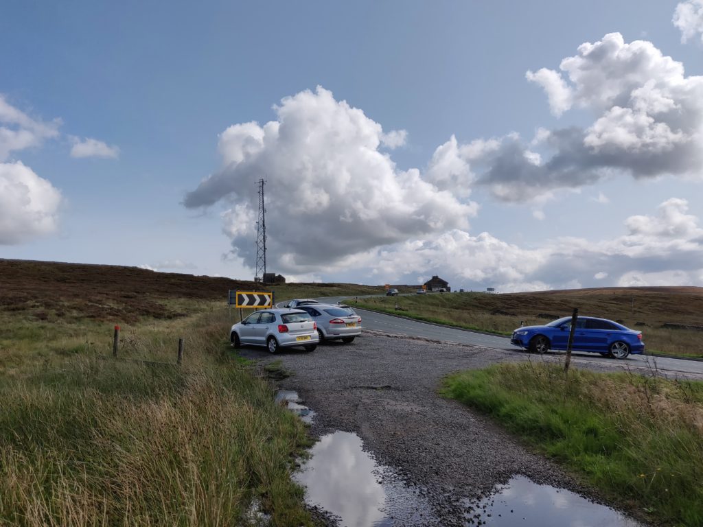Cars parked in gravel layby off road surrounded by moorland